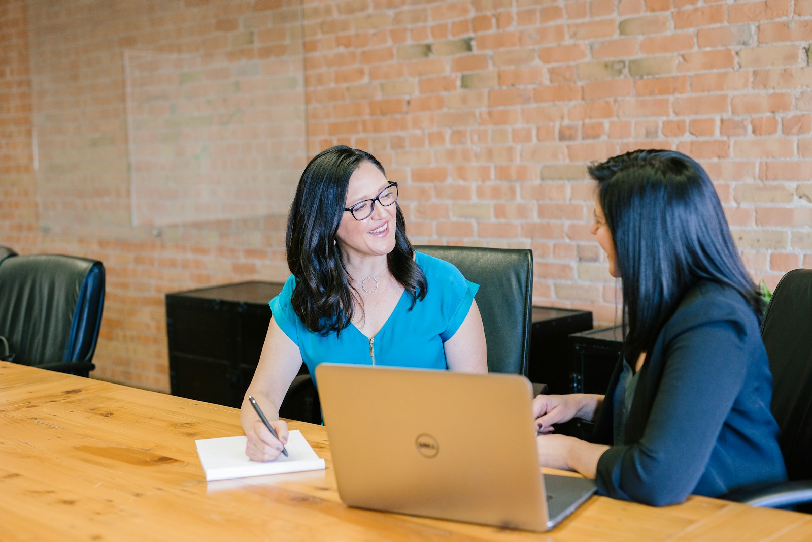 Two colleagues reviewing work together at a wooden table with a laptop and notebook.